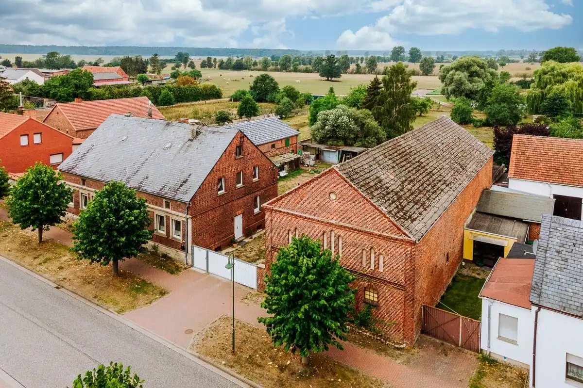Drohnenaufnahme des Dreiseitenhofs aus rotem Backstein mit Scheune in Breddin, dahinter Weiden und Felder