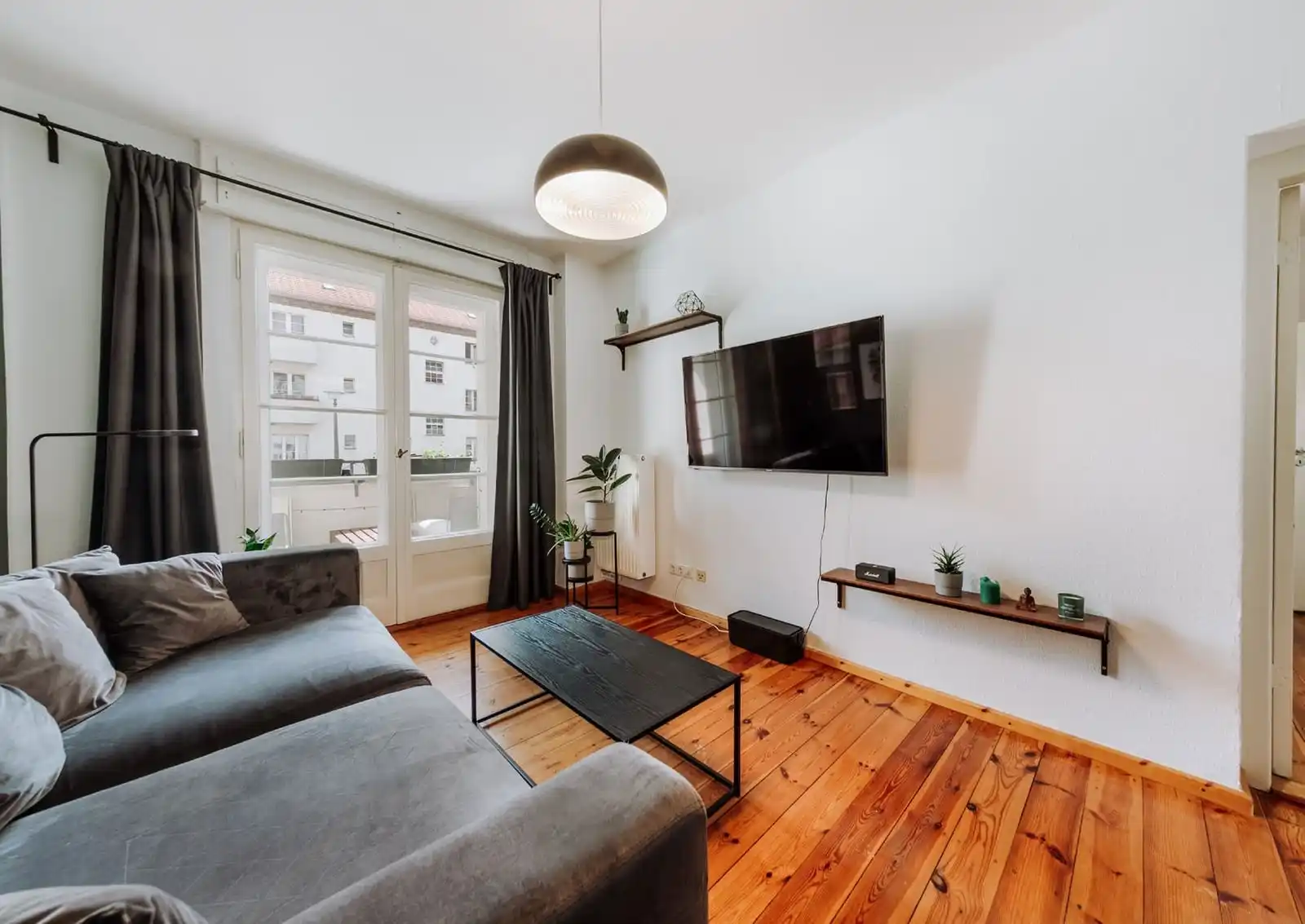 Wohnzimmer mit Dielenboden, grauem Sofa und Fenstertür in der Eigentumswohnung in Berlin-Adlershof