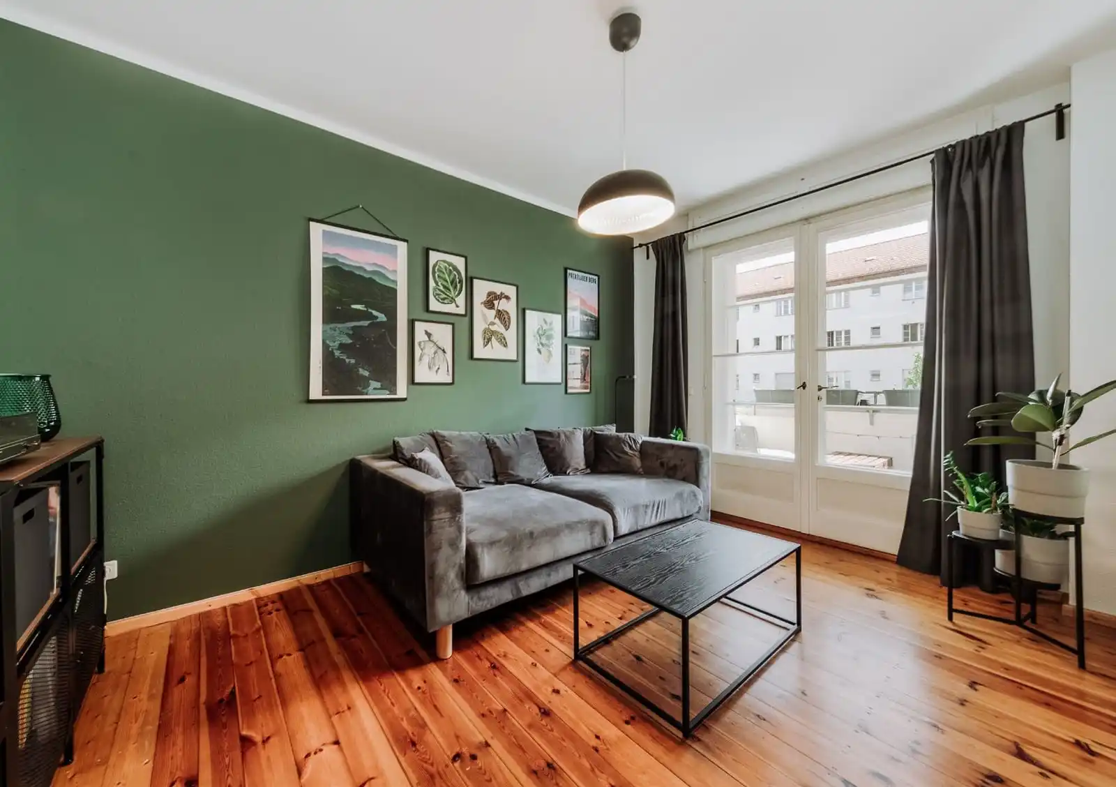 Wohnzimmer mit grüner Wand, Bildern und Dielenboden in der Eigentumswohnung in Berlin-Adlershof